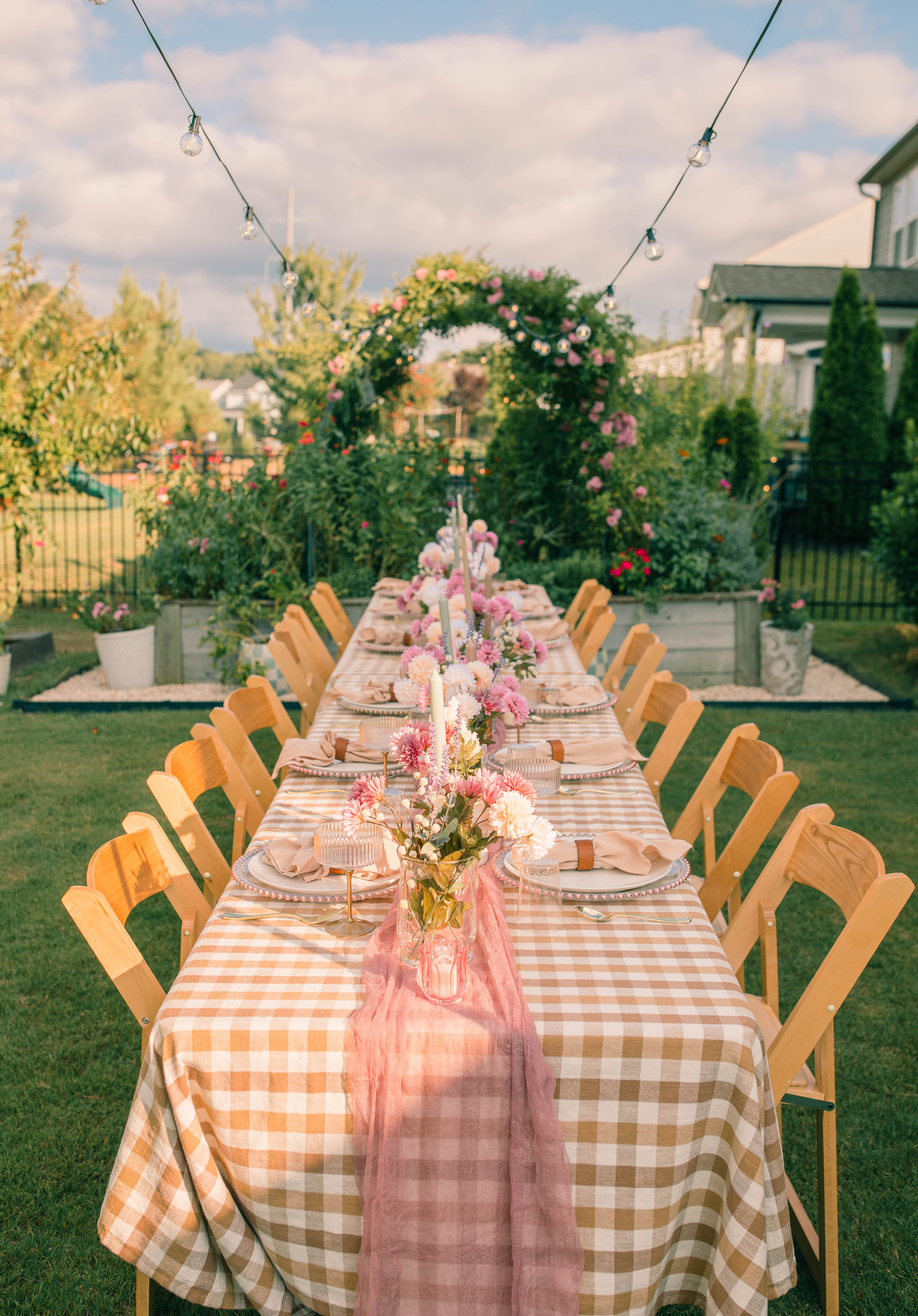 Summer garden dinner party tablescape with pink flowers, gingham tablecloth, candles and string lights